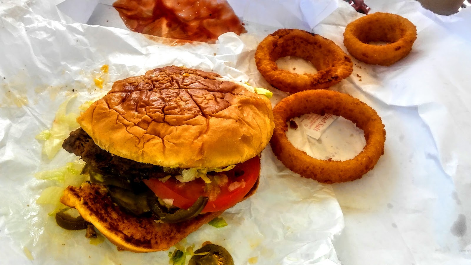 Cheeseburger with lettuce, tomato and jalape&ntilde;o next to golden onion rings