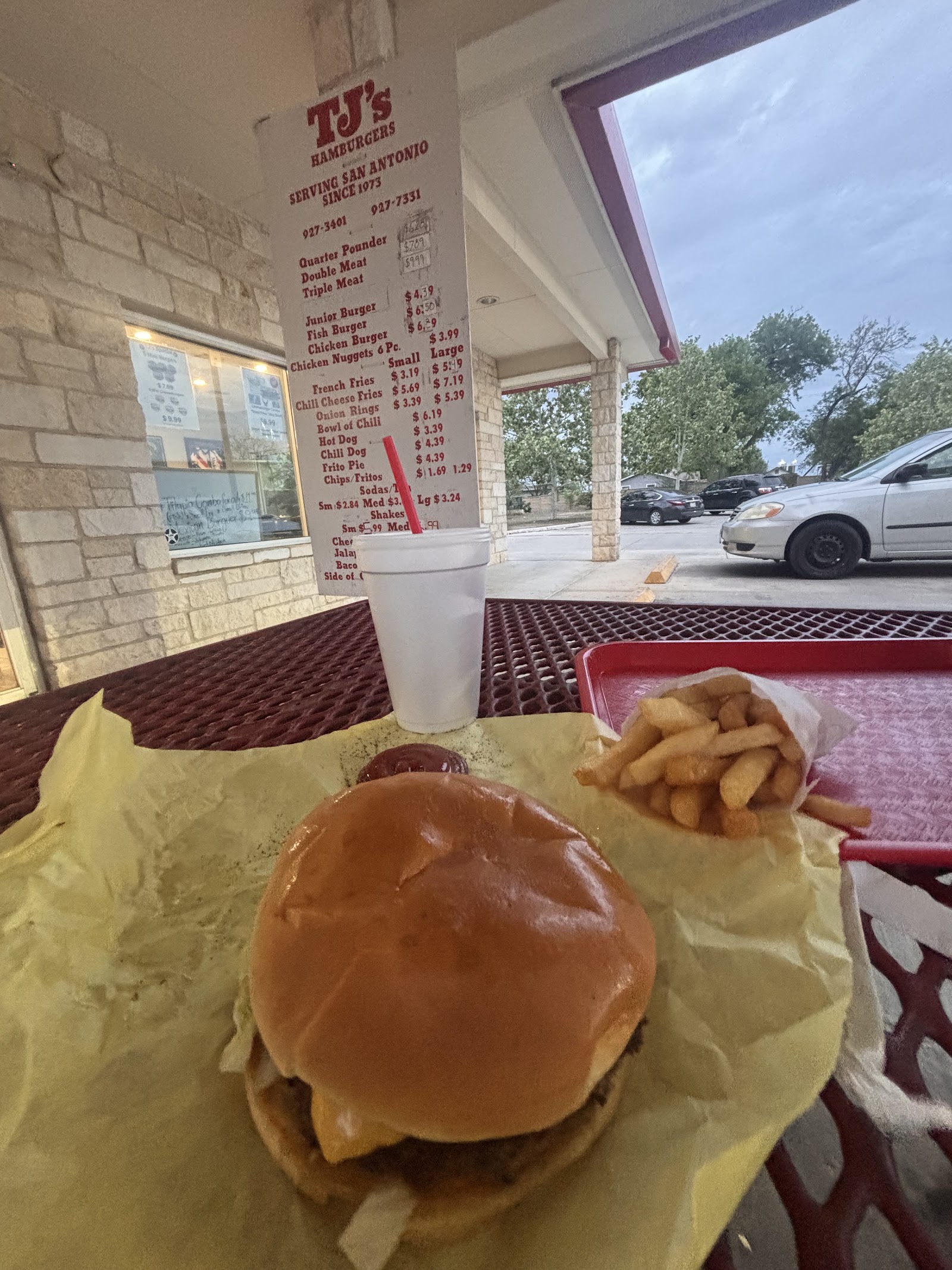 Burger and fries on a red patio table with the menu board in the background