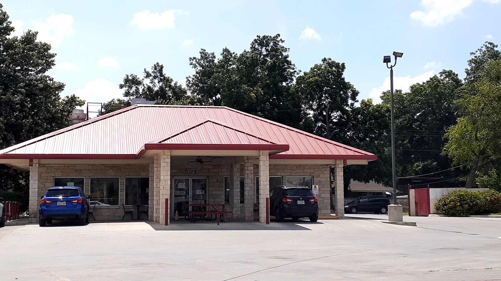 T J's Hamburgers stone storefront with red picnic tables under the covered patio